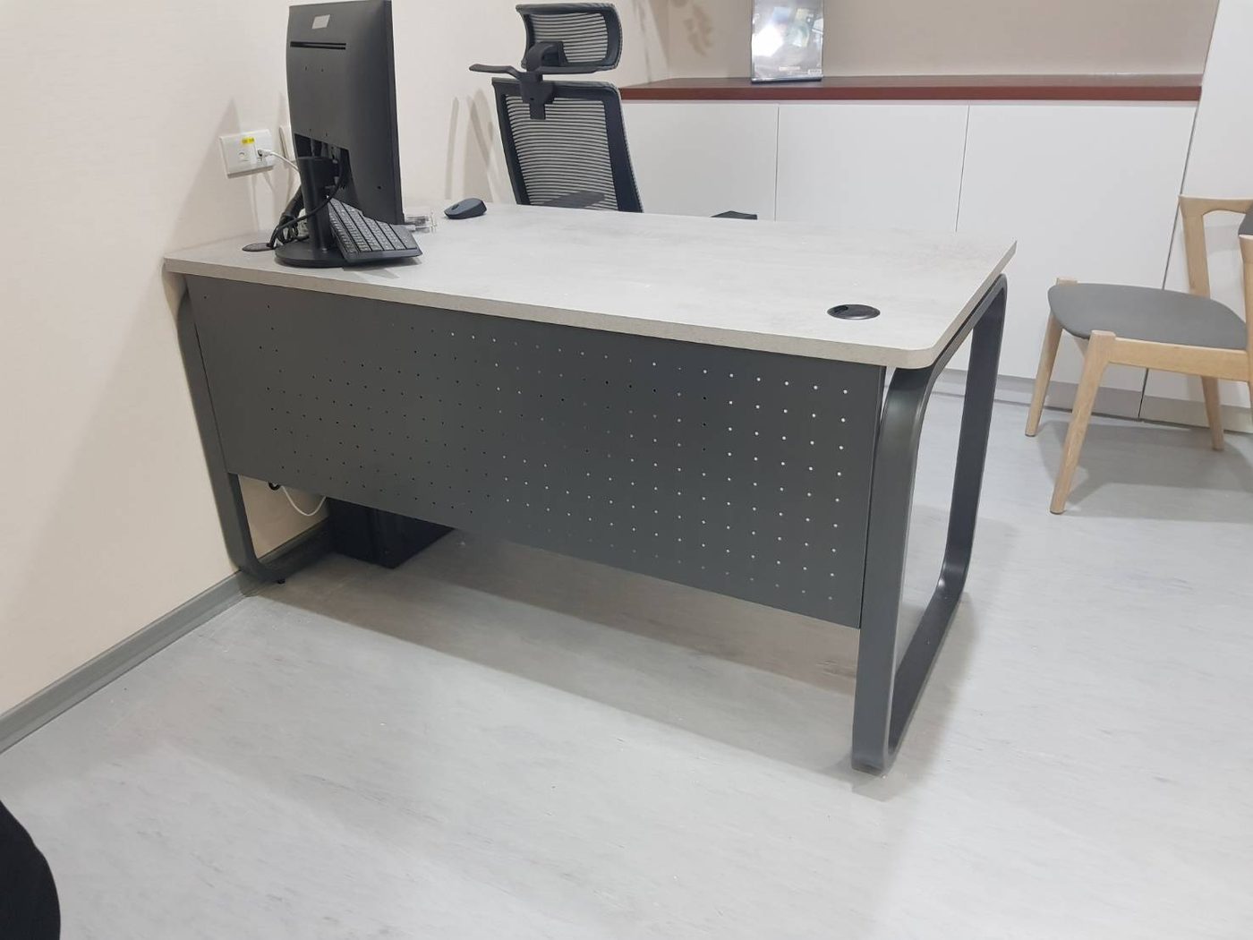 深灰色桌腳工作桌，正面下方深灰檔板上滿佈小圓洞